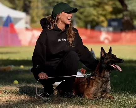 Sarah Dulmage crouching on a sport field beside her Belgian Malinois, Rey.